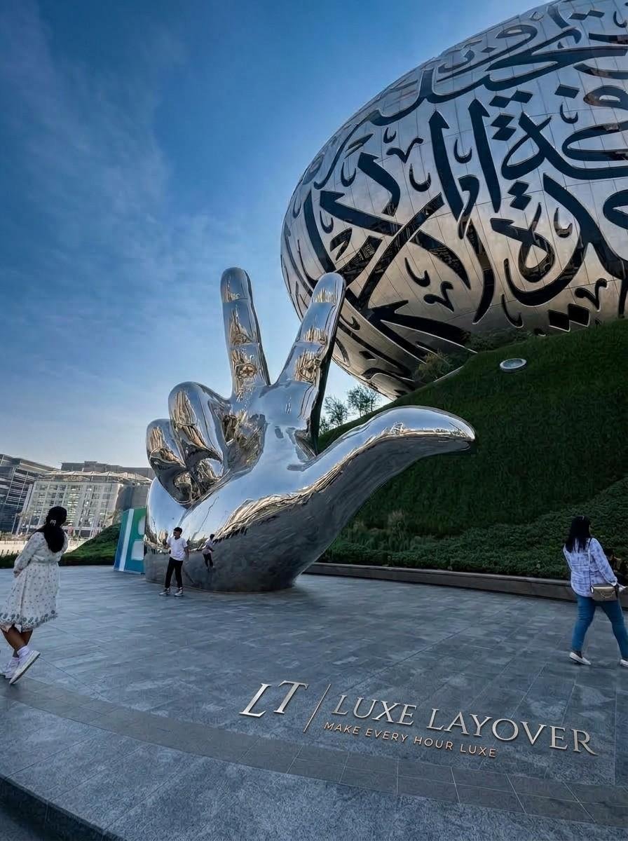 A large stainless-steel sculptural monument shaped like cupped hands, engraved with Arabic