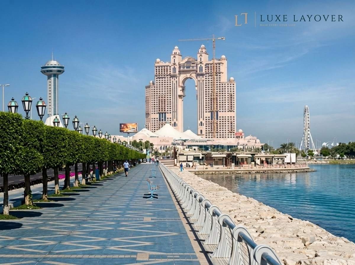 A waterfront promenade lined with palm trees leading toward a hotel and skyline at dusk
