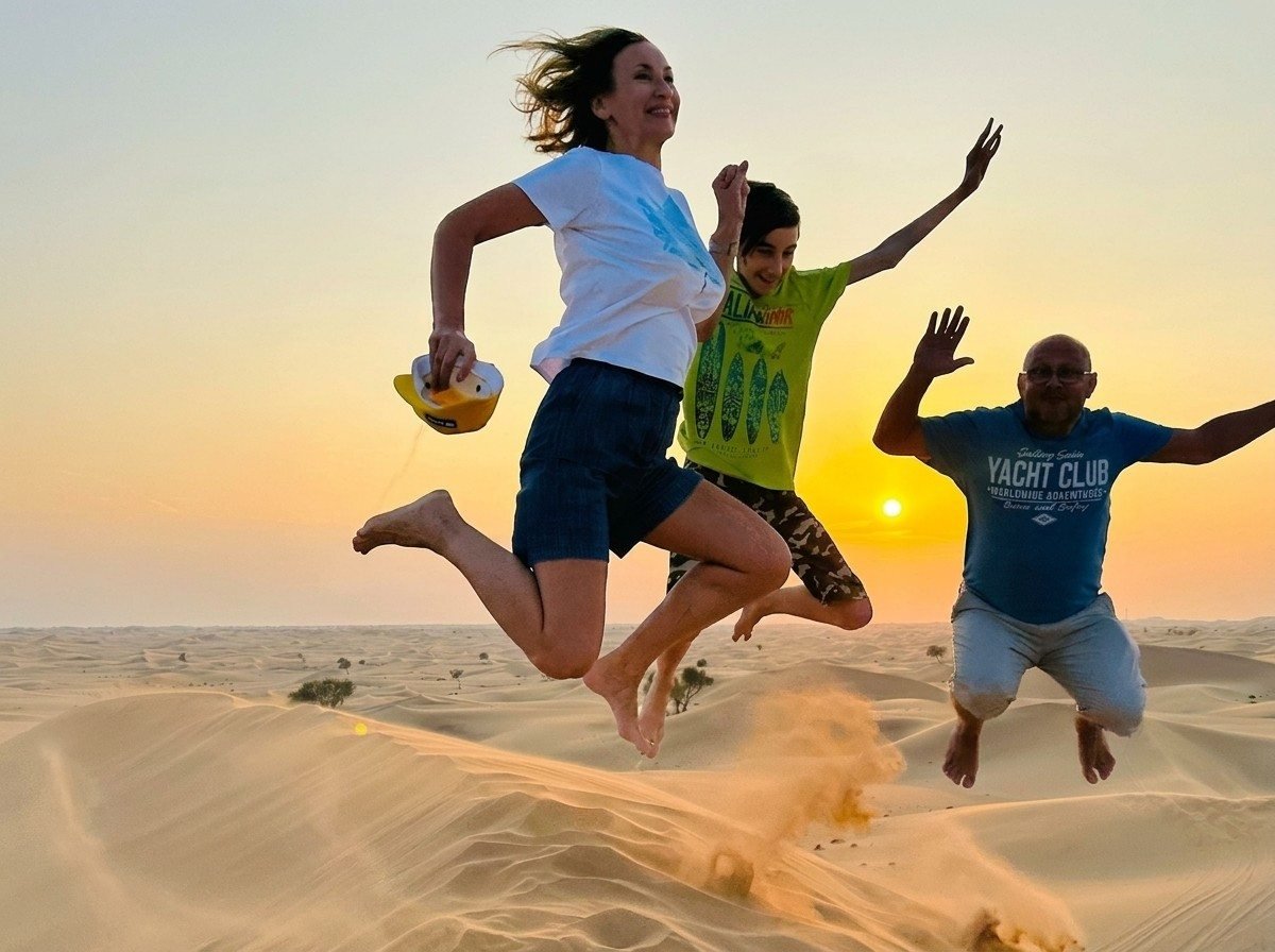 Three friends jumping joyfully on top of a desert sand dune at sunset near Abu Dhabi