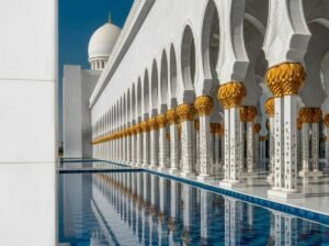 A columned arched corridor beside a reflecting pool inside a mosque complex