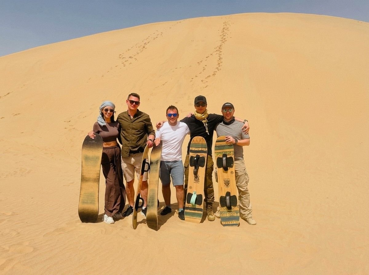 A group of friends posing with sandboards on top of a desert dune