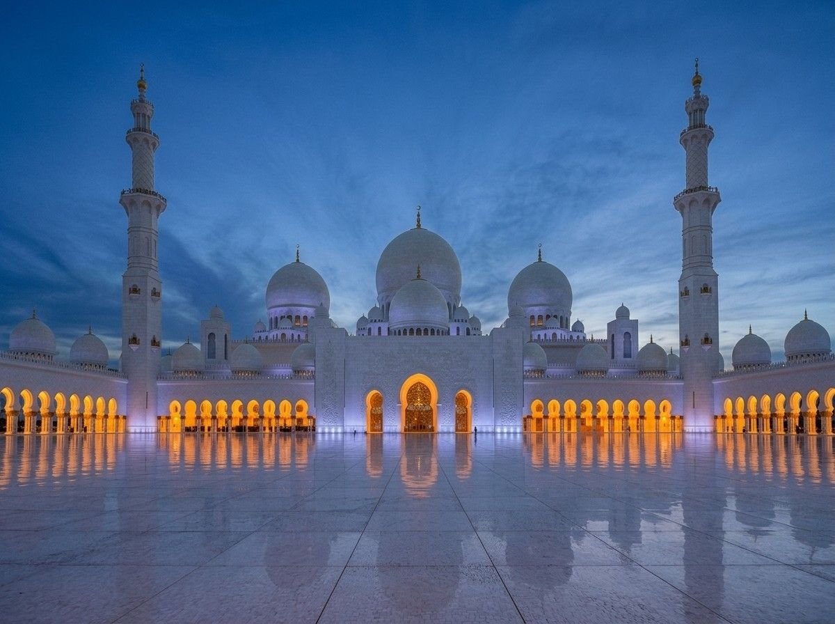 Sheikh Zayed Grand Mosque's domes and minarets illuminated in warm light at dusk