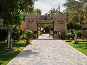 A stone pathway leading through gardens to a heritage village entrance