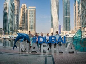 A group of visitors posing beside a large Dubai Marina sign with the skyline behind them