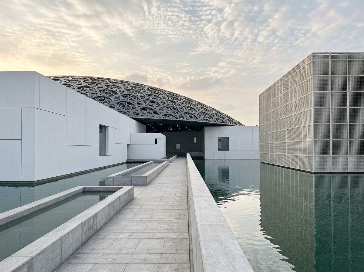A minimalist white walkway leading toward the Louvre Abu Dhabi's dome structure over water