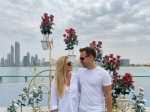 A couple posing together in a rose garden with the Abu Dhabi skyline behind them